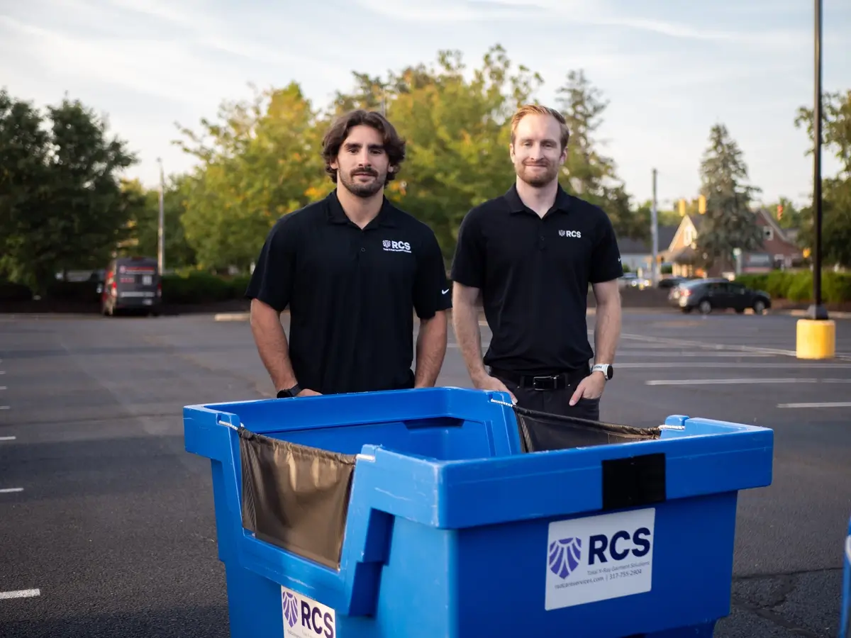 Two RCS Employees standing next to a garment delivery bin